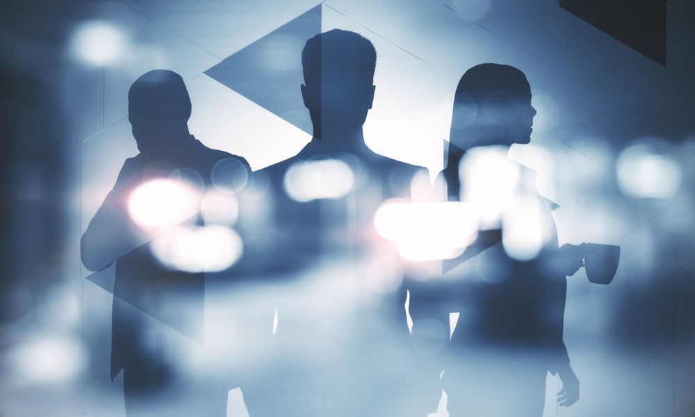 Three business professionals in silhouette standing against a blue-toned abstract background with bright, blurred light spots.