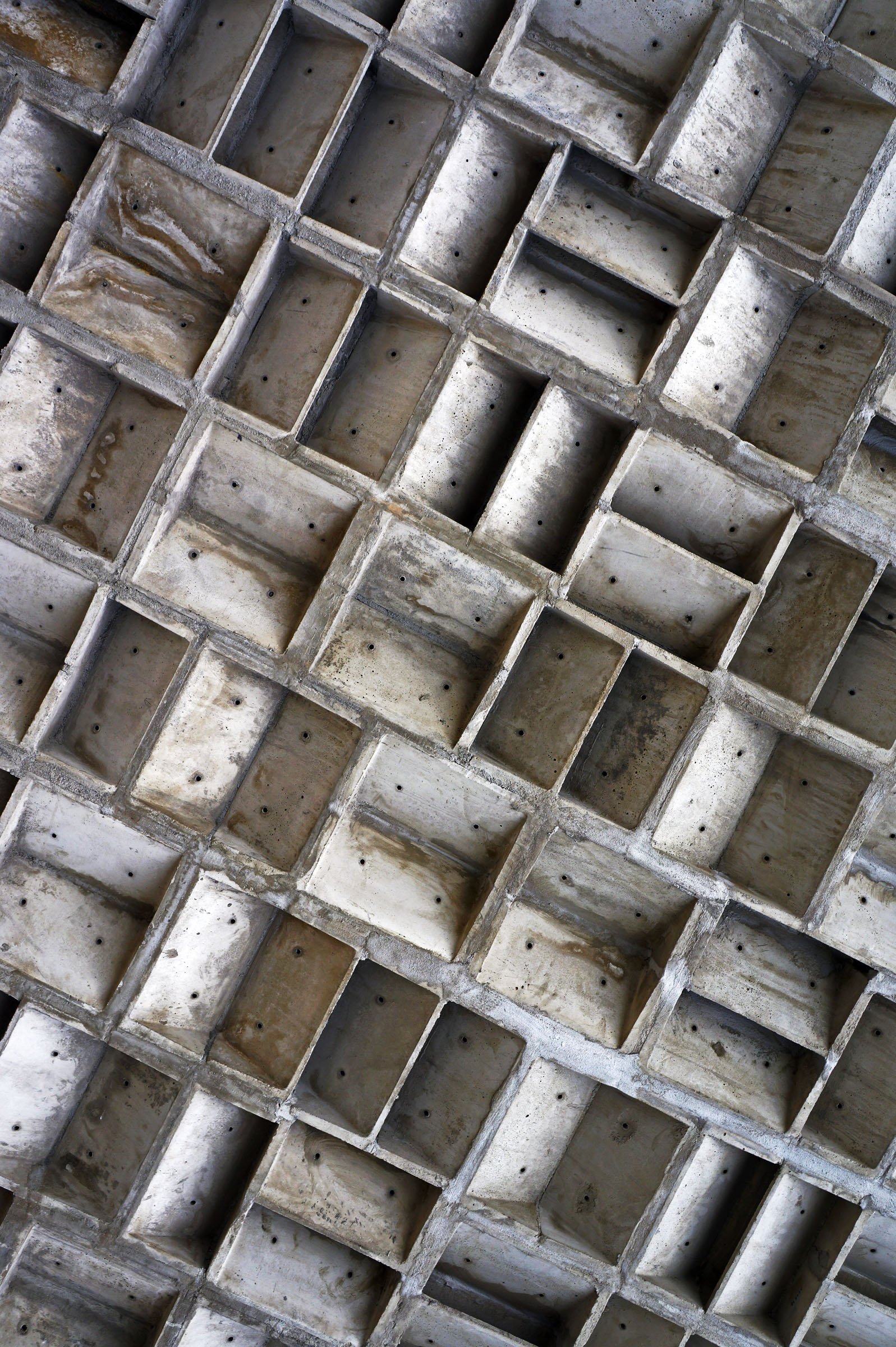 Close-up view of a geometric concrete ceiling with a pattern of square and rectangular recessed blocks arranged diagonally.
