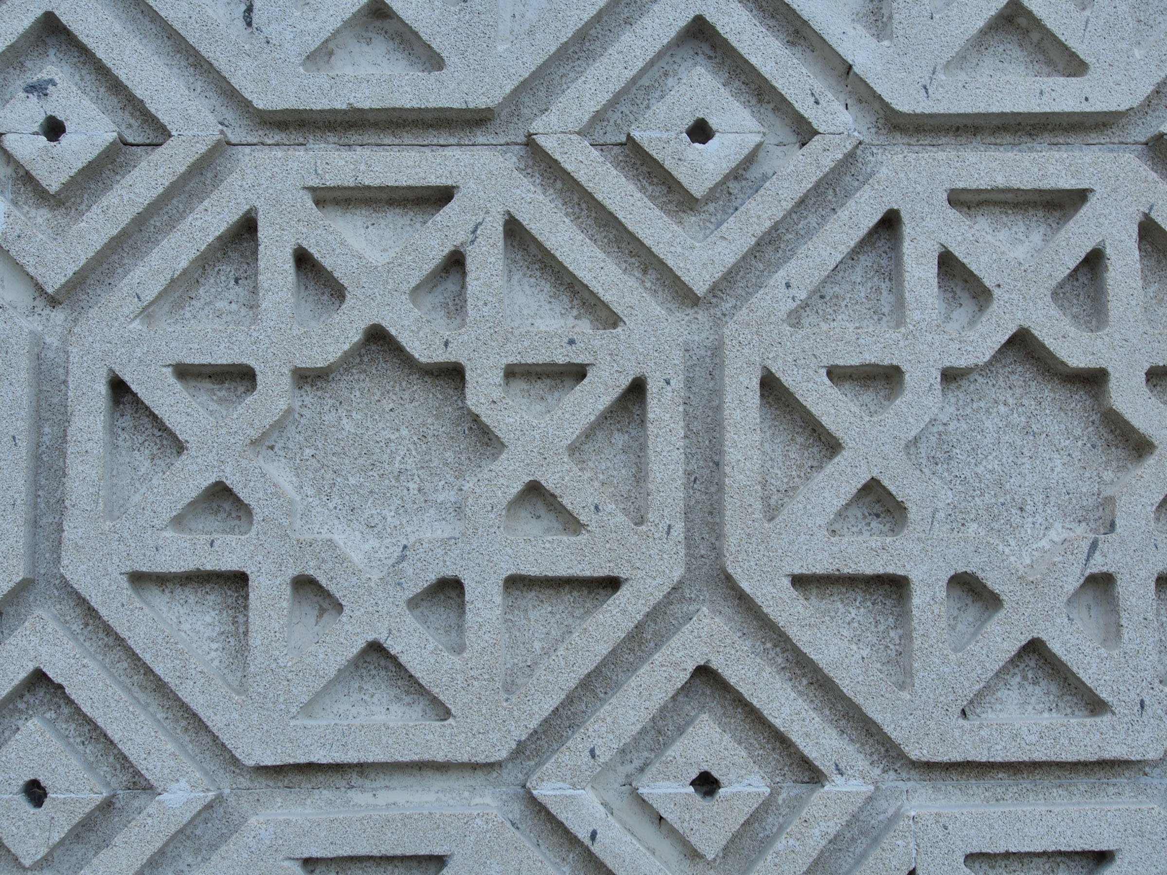 Close-up of a concrete wall featuring a repeating geometric pattern with octagonal shapes enclosing star-like designs, and smaller diamond shapes between them.