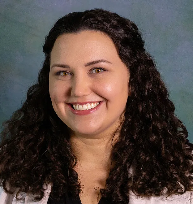 Smiling woman with long curly dark hair against a muted blue-green background.