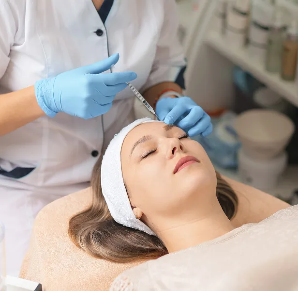 A woman receiving a cosmetic injection on her forehead from a medical professional wearing blue gloves.