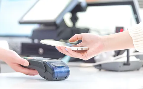 Person using a smartphone to make a wireless payment on a card reader terminal at a counter.