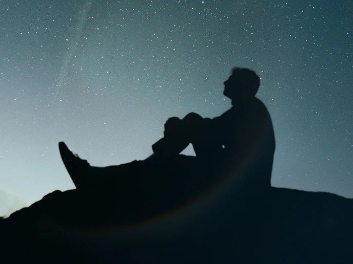 Silhouette of a person sitting on a rock looking at a starry night sky.