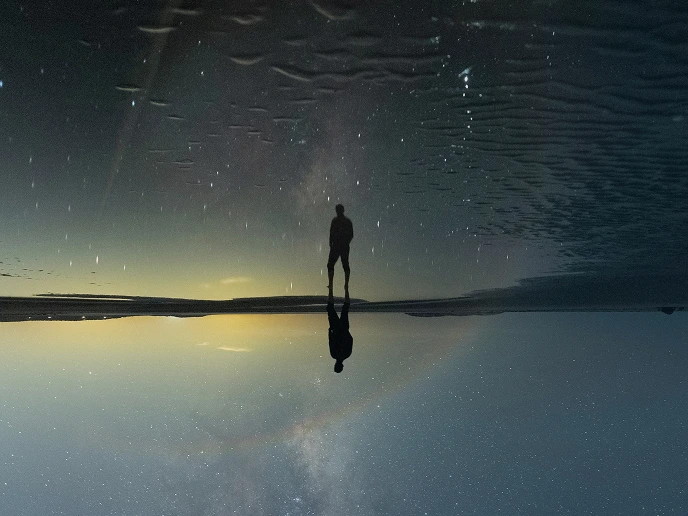 Silhouette of a person standing on a reflective surface under a starry night sky with the Milky Way visible.