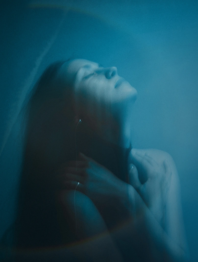 Blurred portrait of a woman with eyes closed and head tilted back, bathed in blue light.