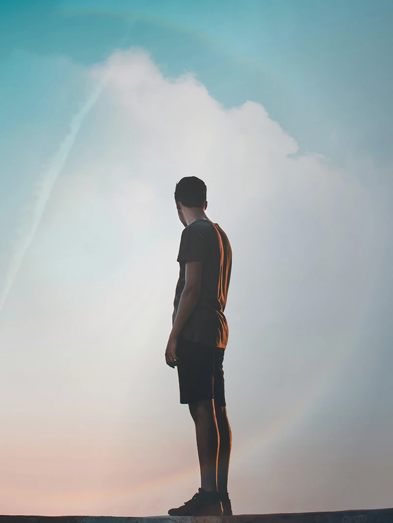 Silhouette of a person standing and looking to the side against a cloudy sky during sunset.