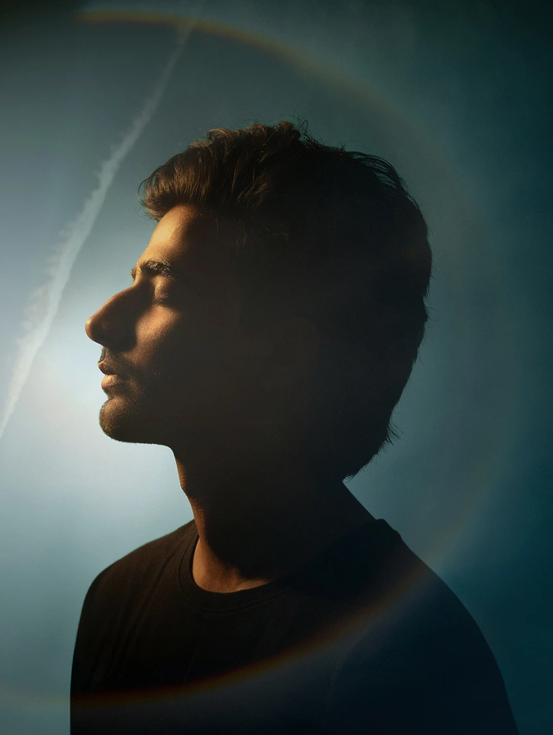 Side profile of a man with closed eyes illuminated softly against a dark background with a circular light halo effect.