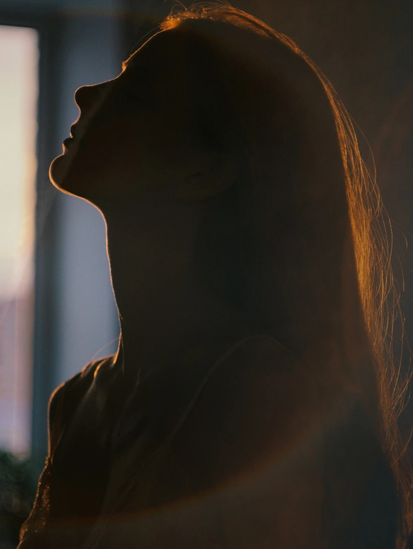 Silhouette of a woman with her head tilted back, illuminated by soft backlighting highlighting her hair and profile.