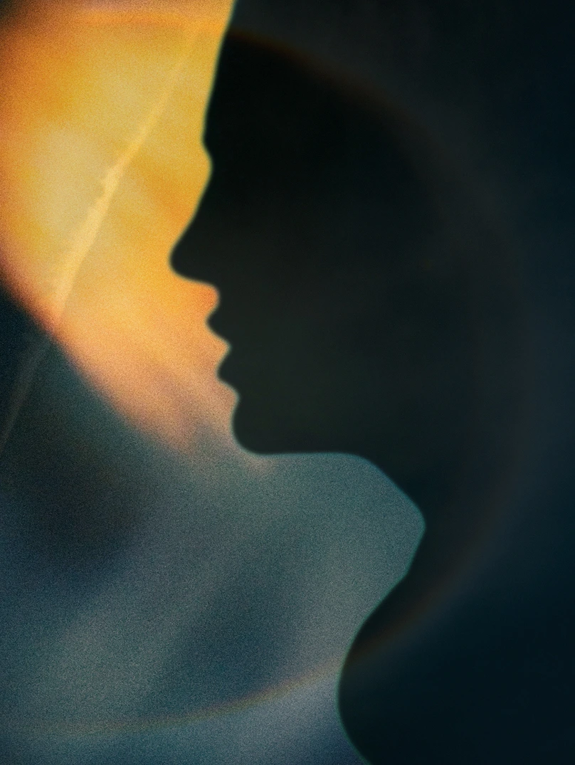 Silhouette profile of a person's face and neck against a blurred warm light background.