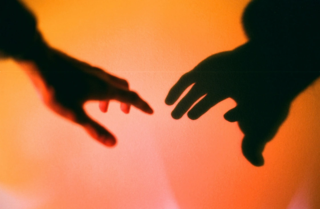 Silhouettes of two hands reaching towards each other against an orange background.