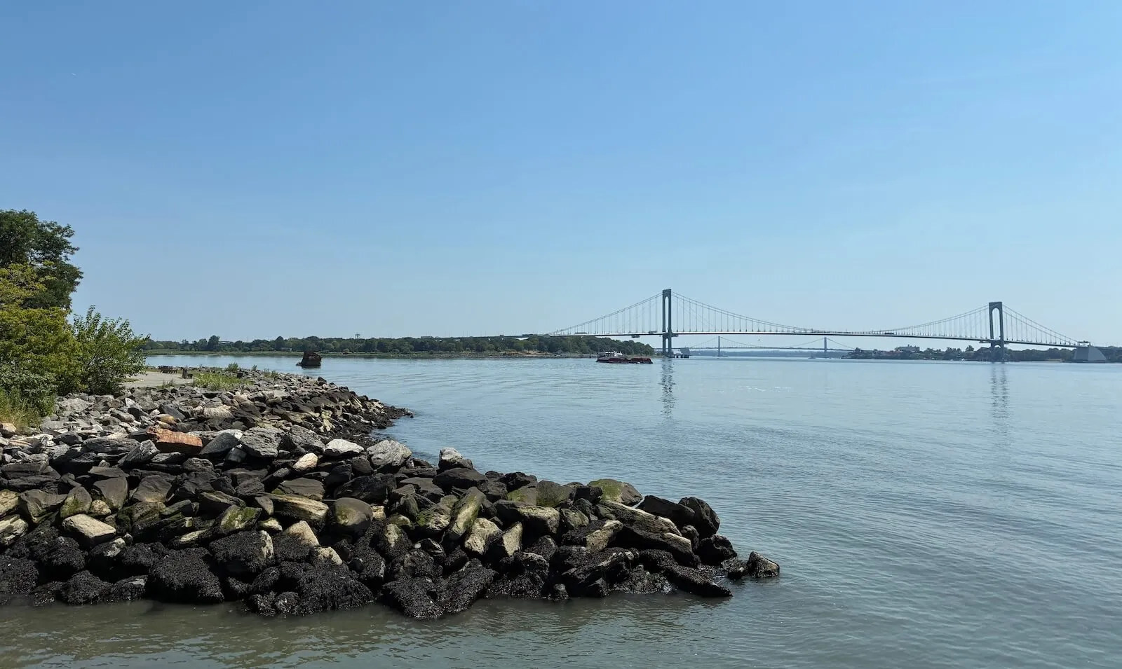 Rocky shoreline at Soundview Park with a suspension bridge spanning the water beyond