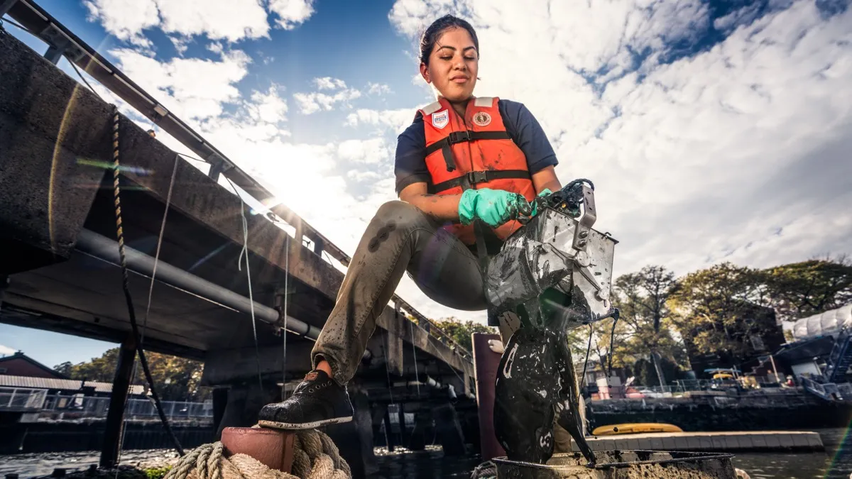 Student in a life vest emptying a mucky oyster cage into a bin at the waterfront