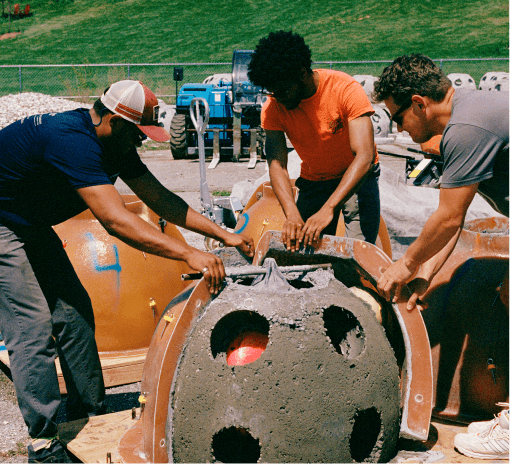 Three workers packing concrete into a dome-shaped reef ball mold