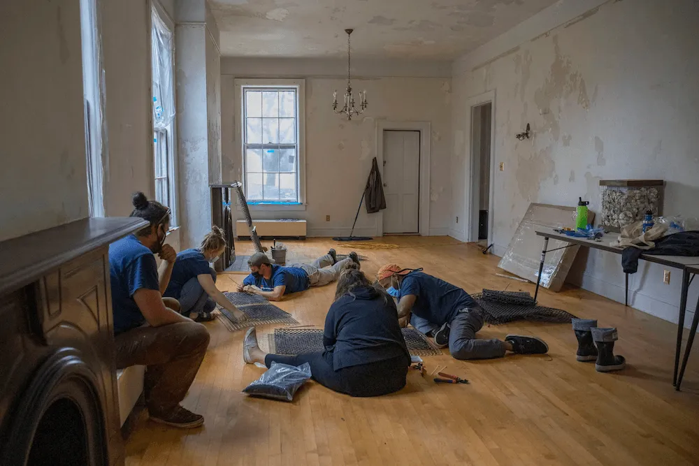 Volunteers work with wire mesh panels on the floor of a historic house under renovation
