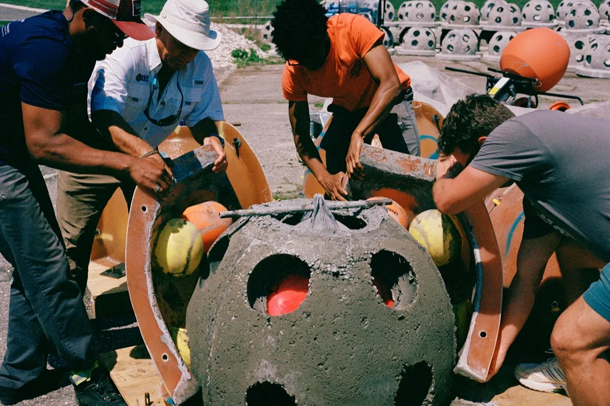A team removes the fiberglass mold from a newly cast reef ball dotted with holes