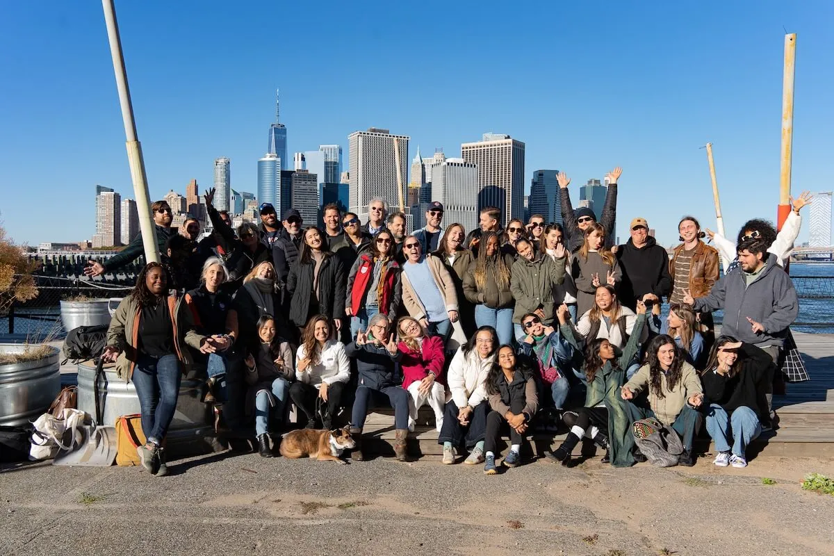 Volunteers posing together on the Brooklyn waterfront with the Lower Manhattan skyline behind