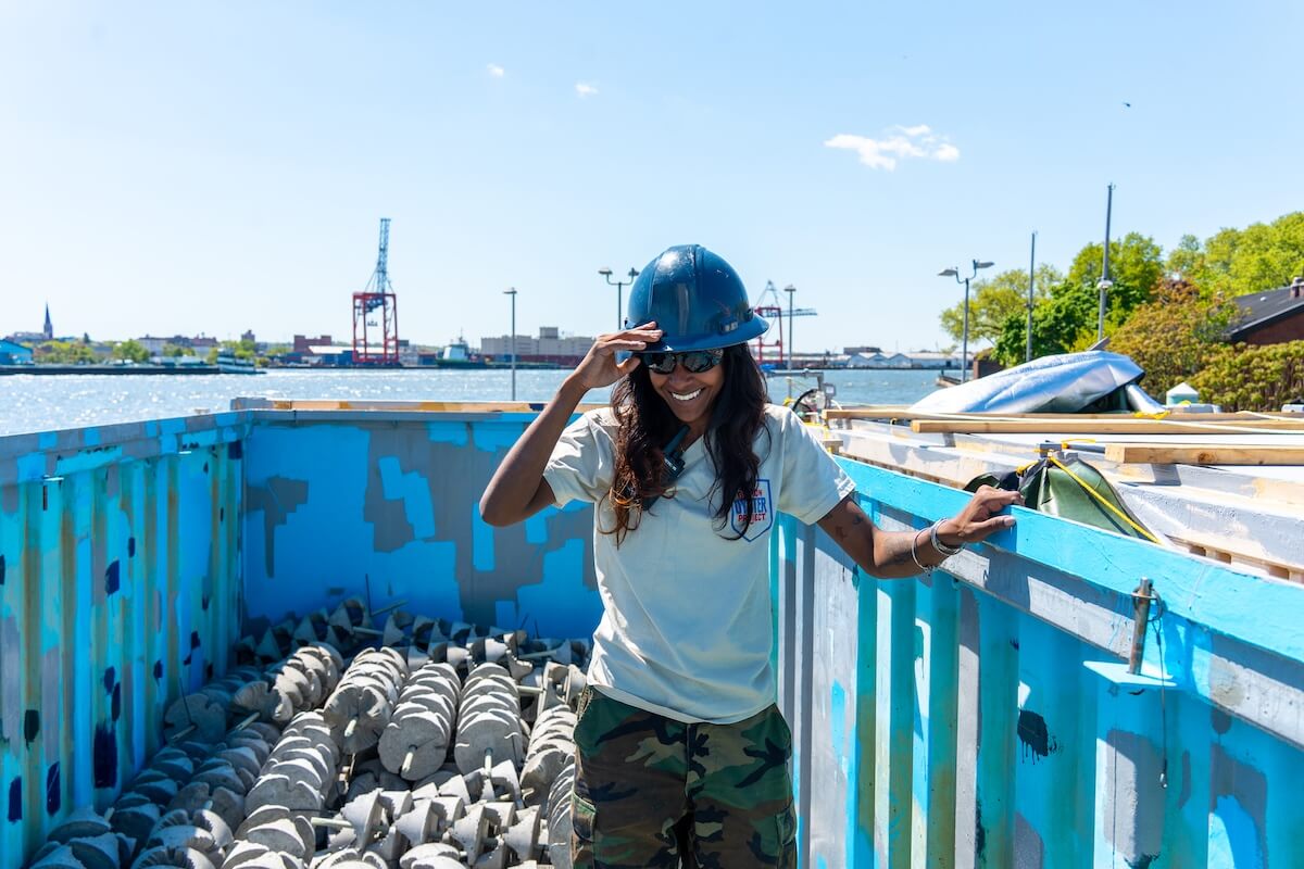Smiling crew member in a hard hat standing in a barge bin of concrete reef structures