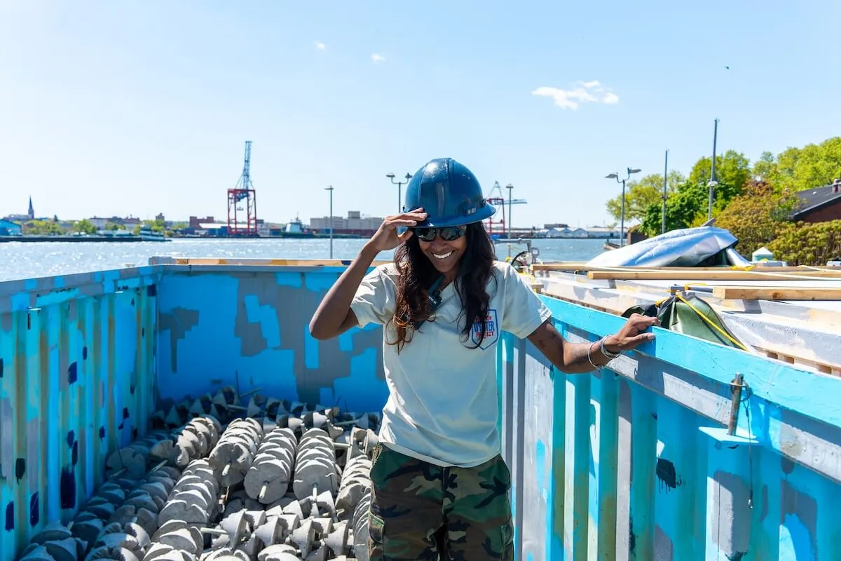 Smiling crew member in a hard hat standing in a barge bin of concrete reef structures