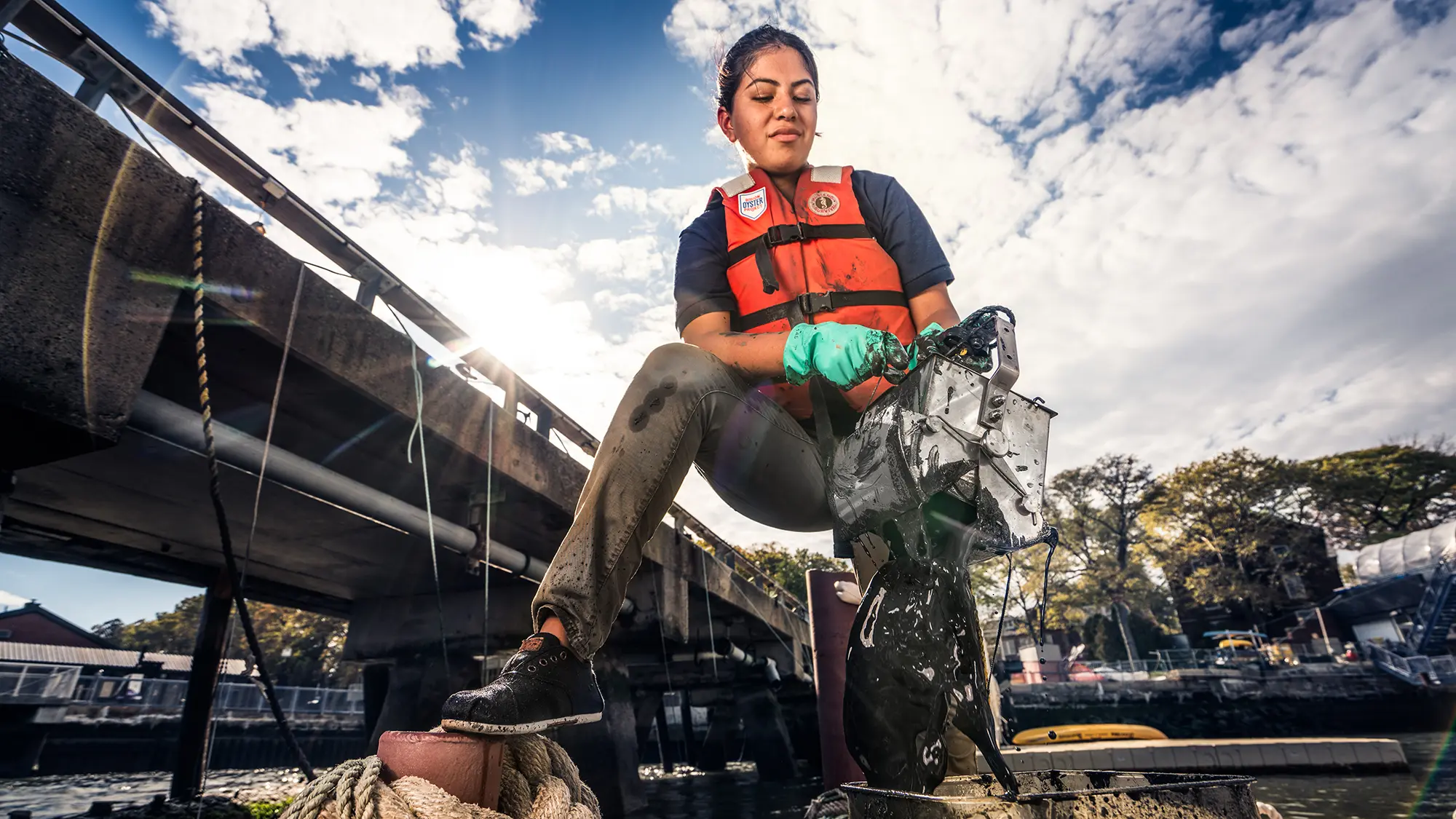 Woman in a life vest hauling a mud-covered oyster research station from the water