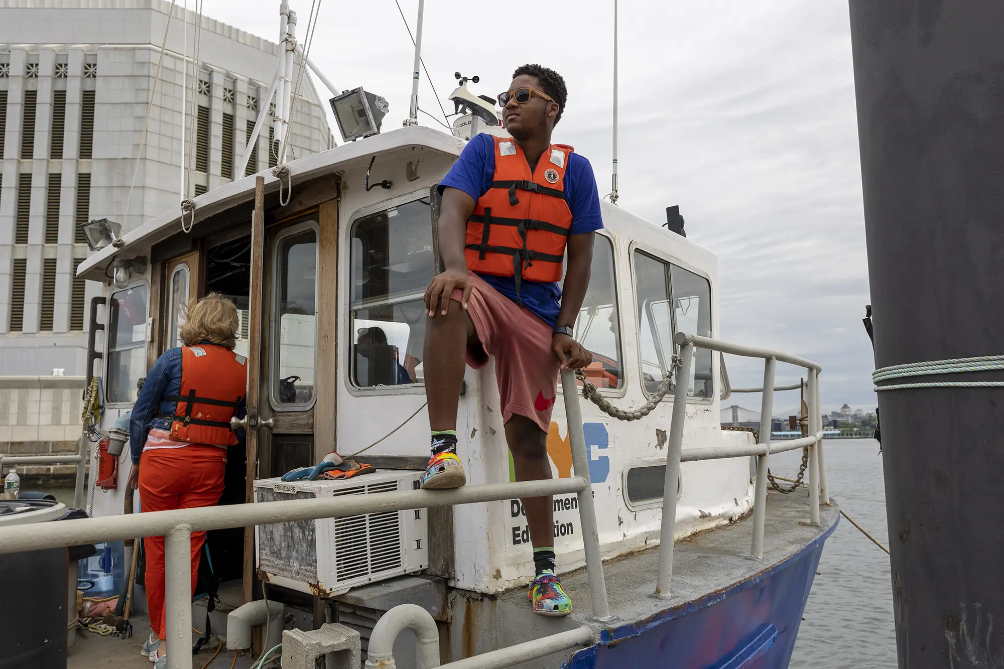 Student in a life vest perched on the rail of a NYC Department of Education boat