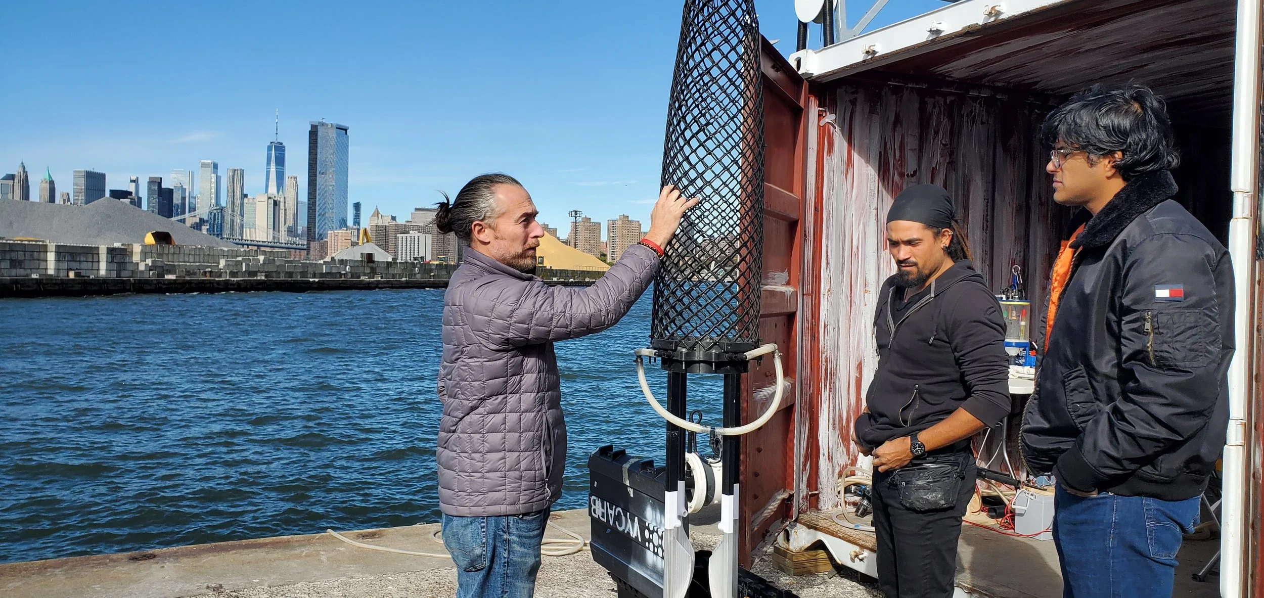 Researchers examining a Vycarb water chemistry unit on a pier with the Manhattan skyline behind
