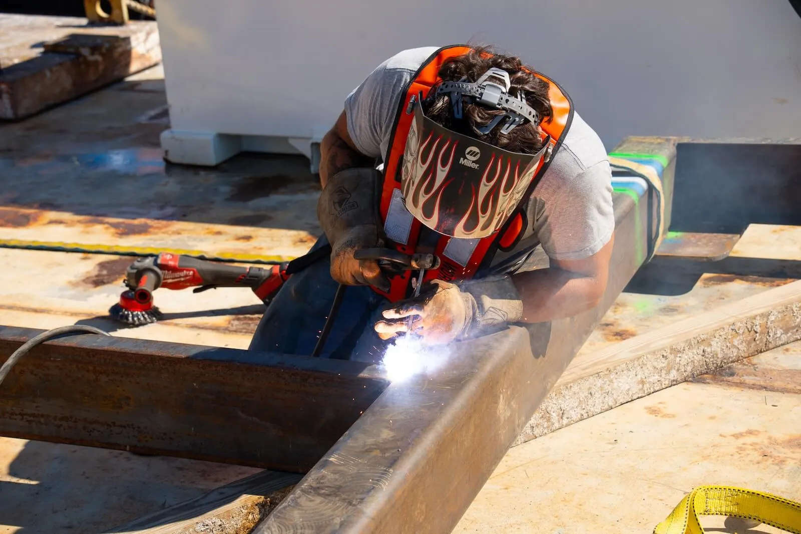 A welder in a flame-painted mask joins steel framing for reef infrastructure on a barge deck