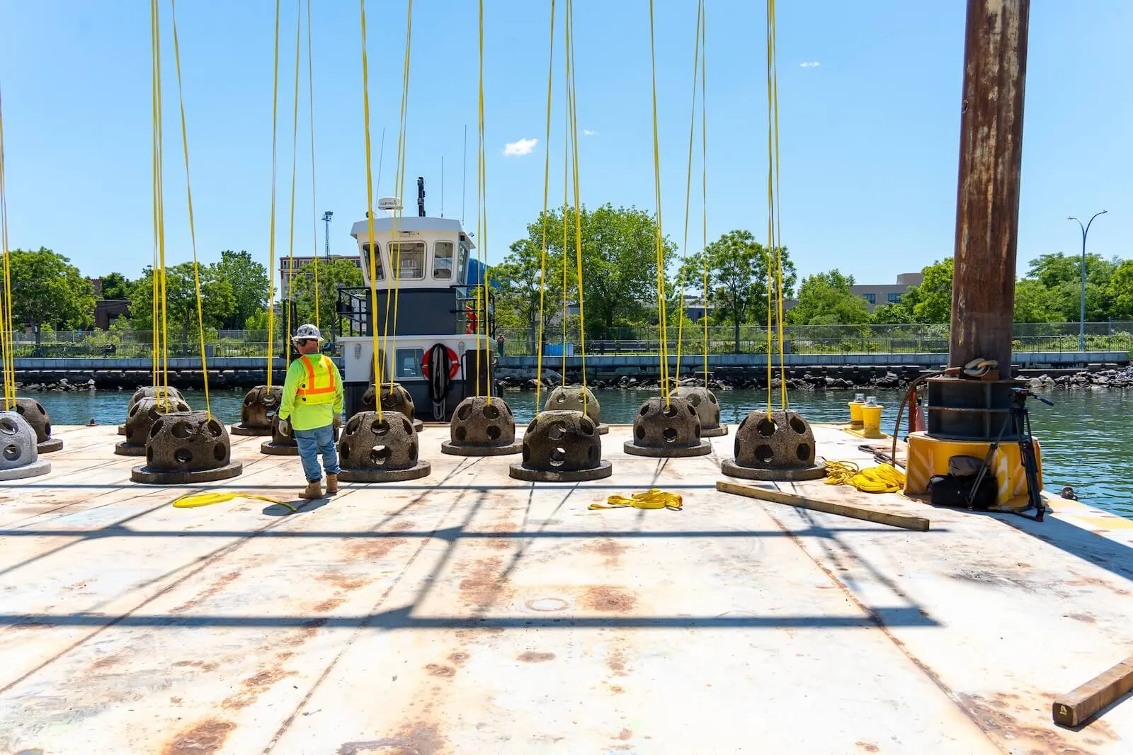 Worker walks a barge deck lined with reef balls rigged to yellow lifting slings