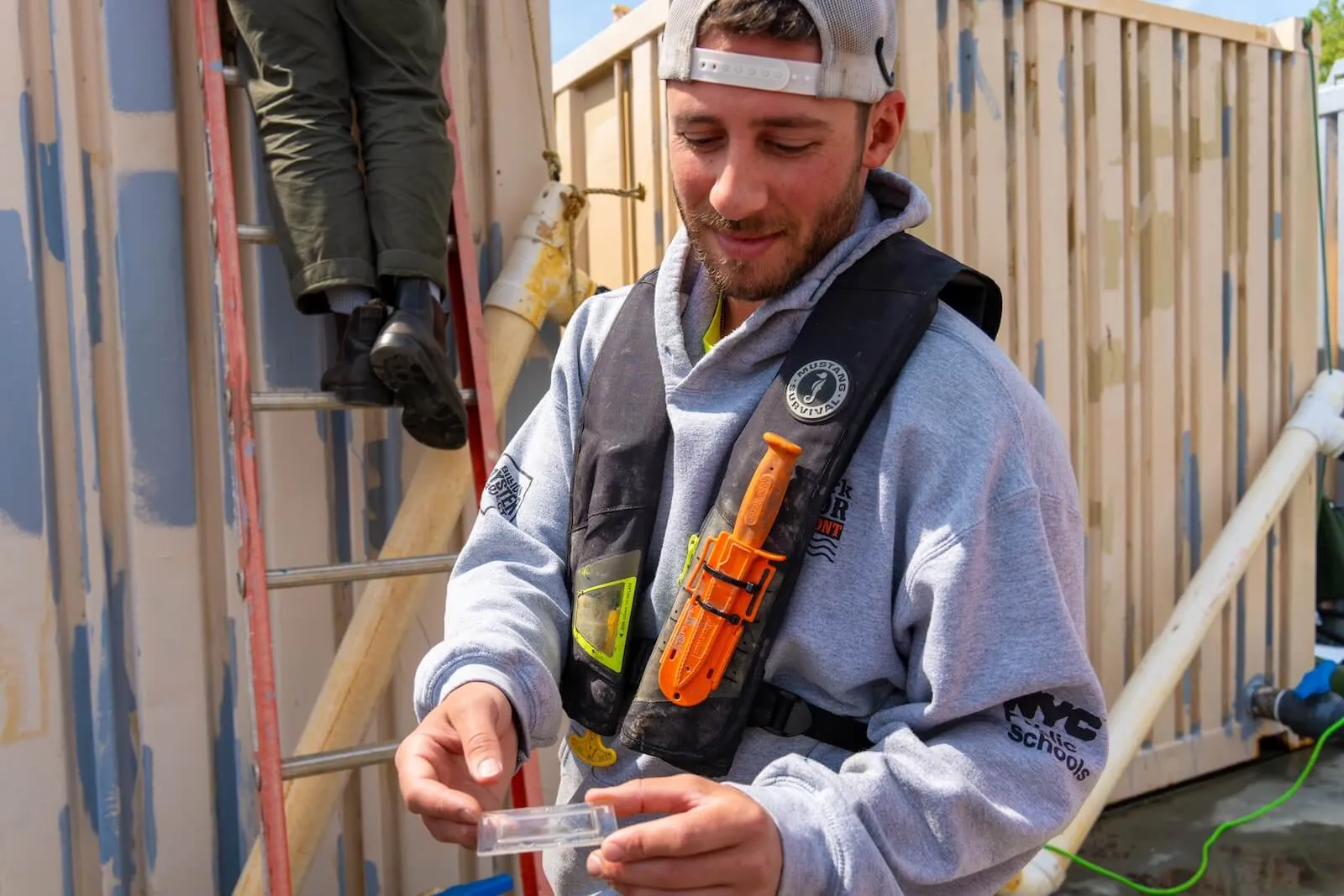Worker in a life vest examines a small sample container aboard a restoration barge