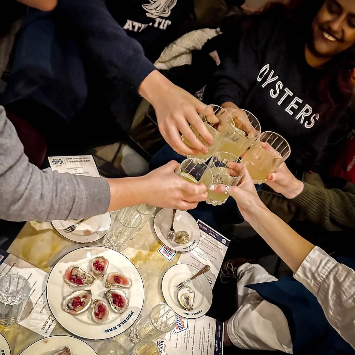 Friends toast cocktails over plates of dressed oysters at a Billion Oyster Project pairing night