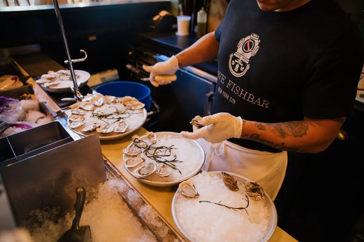 A gloved shucker plates oysters on iced trays at a New York City fish bar