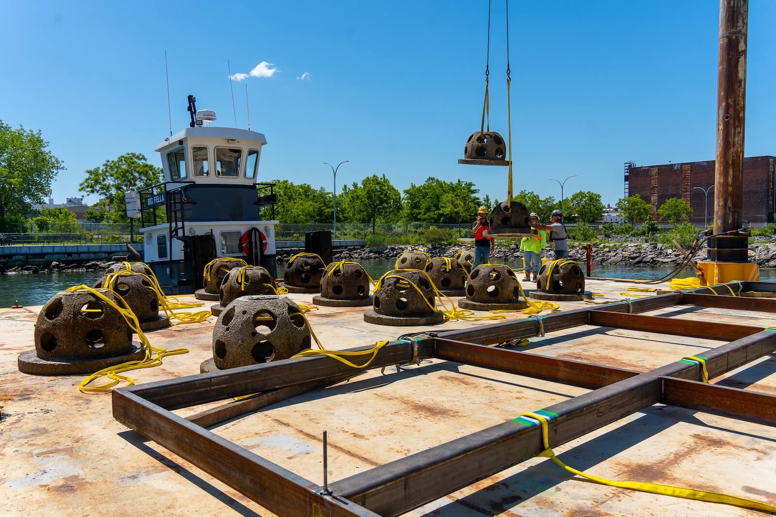 Crane lowering a concrete reef ball onto a barge staged with dozens more
