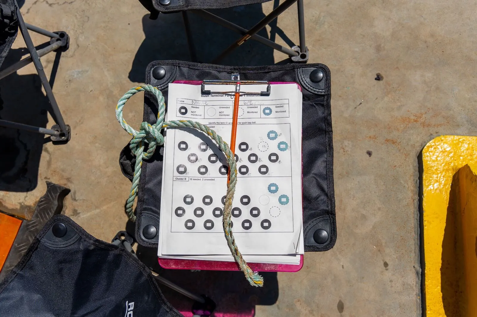 Reef monitoring datasheet on a clipboard beside a knotted rope at a harbor worksite