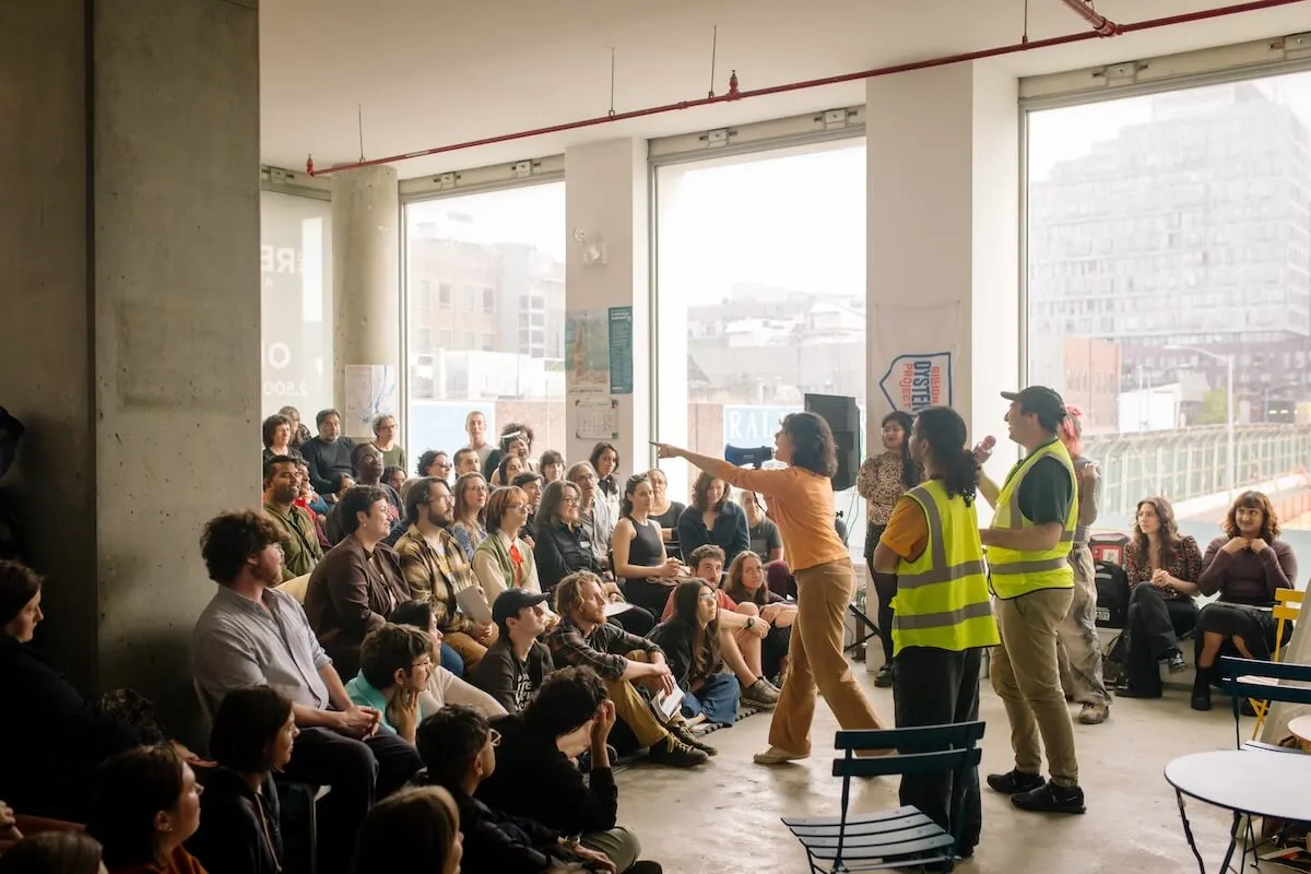 A presenter gestures to a seated crowd at a Billion Oyster Project volunteer gathering
