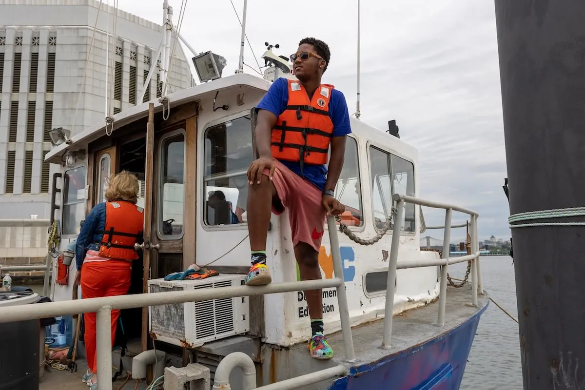A student in a life vest rides the rail of a NYC Department of Education workboat