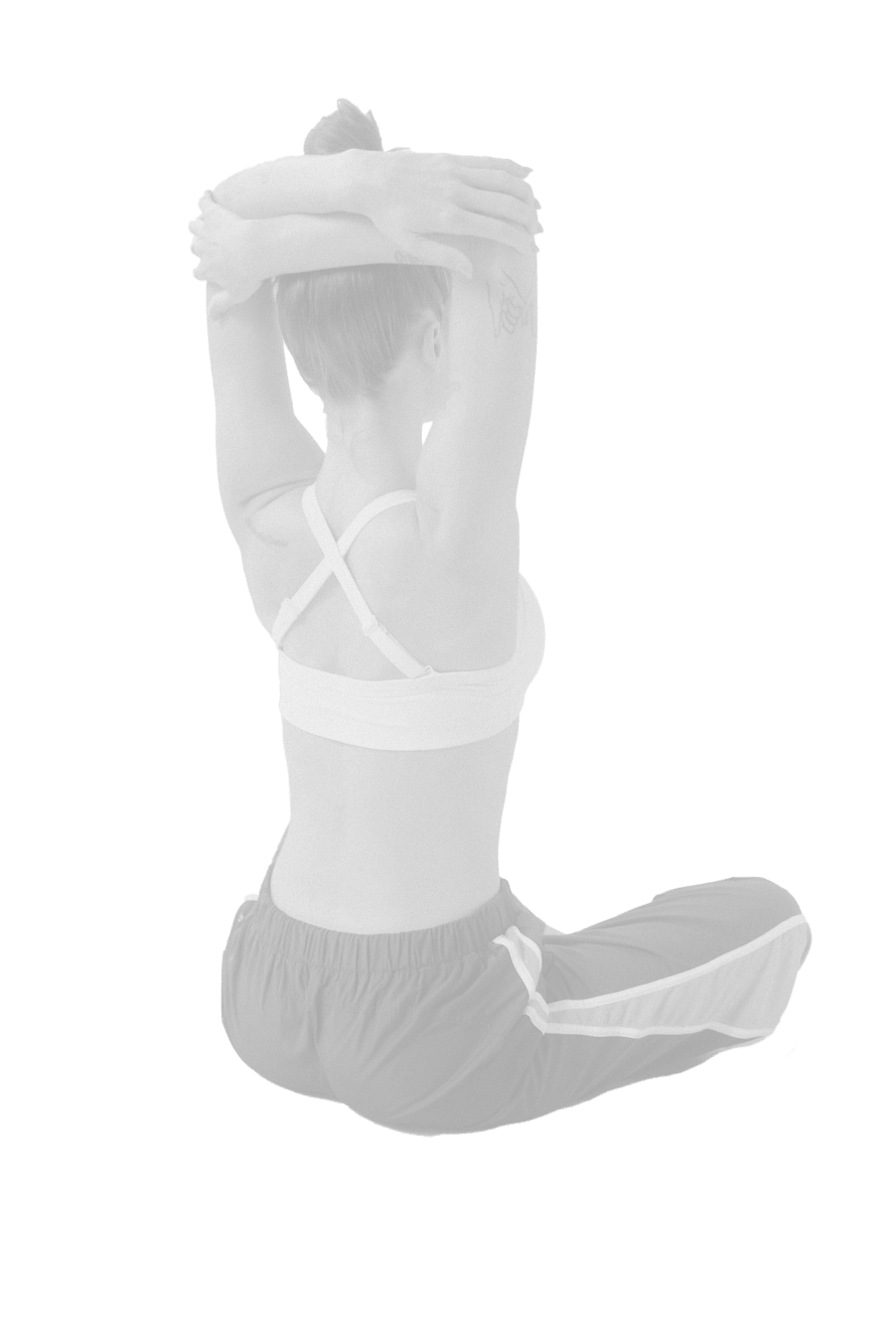 Woman sitting cross-legged wearing sports bra and sweatpants stretching her arms overhead behind her head.