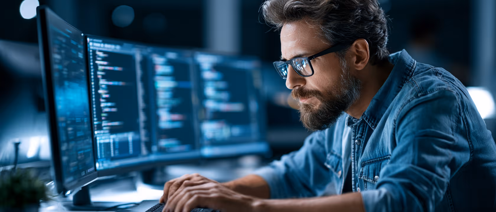 Homme concentré codant sur ordinateur avec plusieurs écrans affichant du code en environnement sombre.