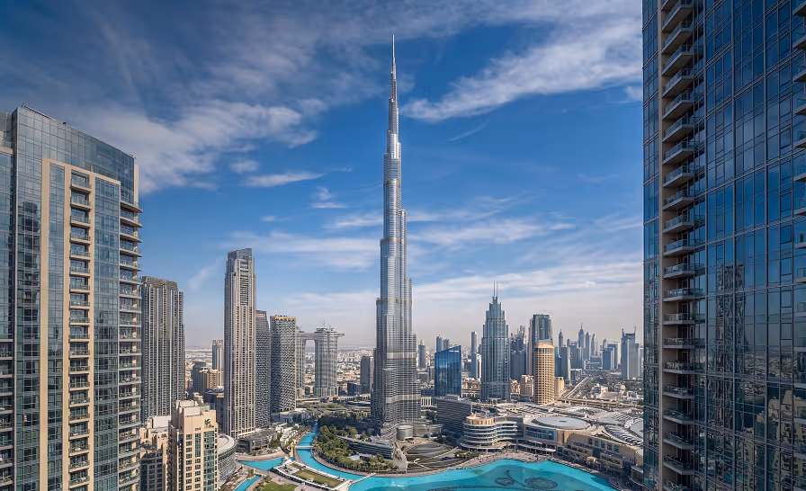 Panoramic view of Dubai skyline featuring the Burj Khalifa tower under a blue sky with scattered clouds.