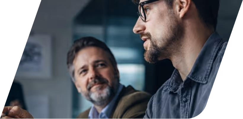 Two men in a work meeting, one with glasses talking while the other listens attentively.