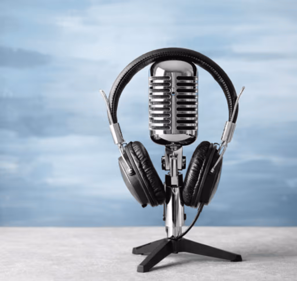 Silver retro microphone with black headphones placed on a gray surface in front of a blurred blue background.