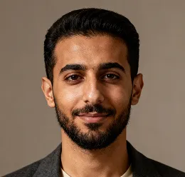 Portrait of a man with dark hair and beard smiling slightly against a plain brown background.