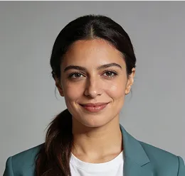 Smiling woman with dark hair tied back, wearing a teal blazer and white top against a gray background.