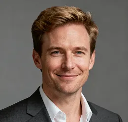 Smiling man with short light brown hair wearing a dark suit jacket and white shirt against a gray background.