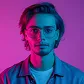 Portrait of a young man with glasses and medium-length hair illuminated by pink and blue lighting.
