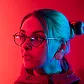 Portrait of a woman with glasses, illuminated by red and blue lighting, looking to the side.