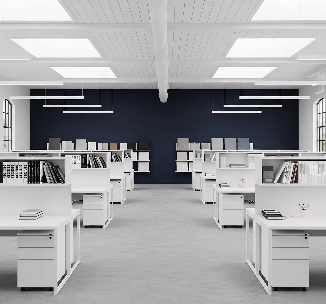 Modern office space with rows of white desks equipped with bookshelves and storage drawers under bright ceiling lights.