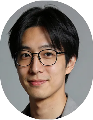 Portrait of a young Asian man with black hair and glasses smiling against a gray background.