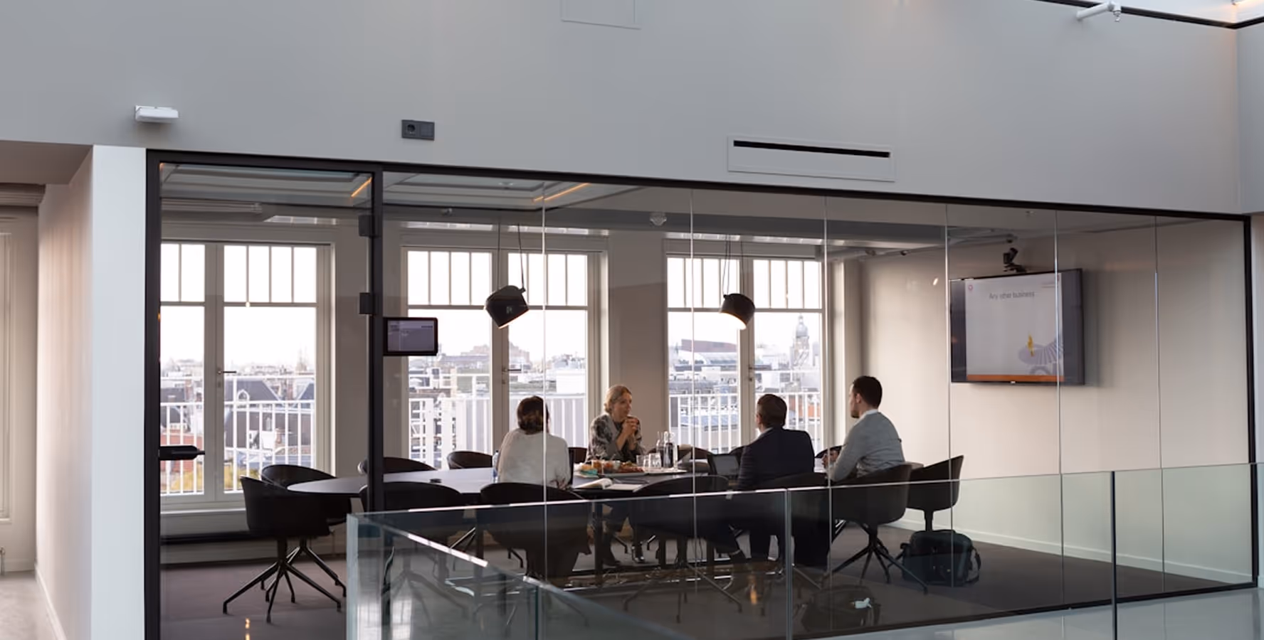 Cuatro personas reunidas alrededor de una mesa en una sala de conferencias con paredes de vidrio y ventanas grandes hacia la ciudad.