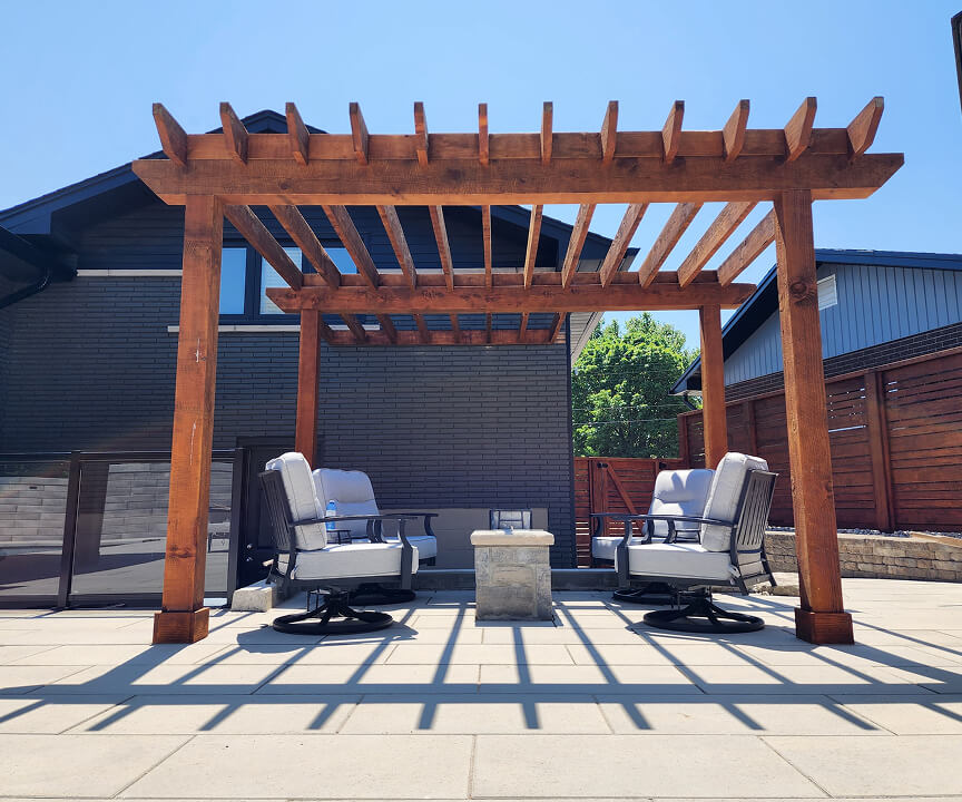 Wooden pergola over outdoor patio with four cushioned swivel chairs and a small stone table in the center.