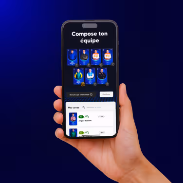 Hand holding a smartphone displaying a fantasy sports app screen with the title 'Compose ton équipe' and player cards arranged for team selection.