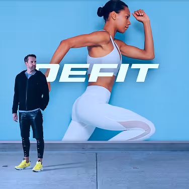 Man in black jacket and yellow shoes standing next to a large blue advertisement featuring a woman in white athletic wear running with the text 'DEFIT'.